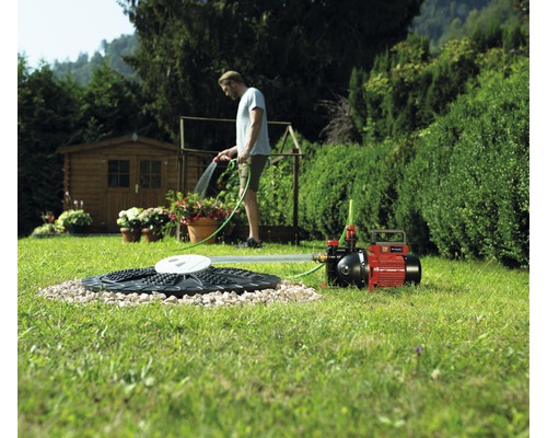 Ein Garten mit einer Zisterne, einer Gartenpumpe und einer Person, die mit einem Gartenschlauch gießt