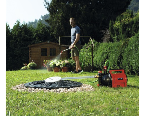Gartenszene mit Mann, der mit einer Gartenpumpe und einem Schlauch Pflanzen bewässert