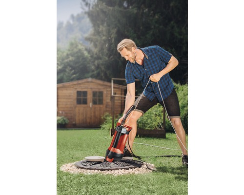 Mann bedient eine Tauchpumpe im Garten zur Entwässerung eines Schachts.