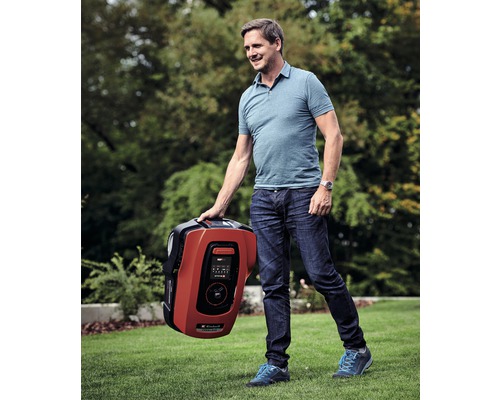 Un homme porte un robot tondeuse dans le jardin.