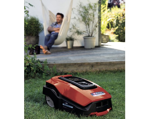 Robot tondeuse dans le jardin avec un homme détendu dans un hamac