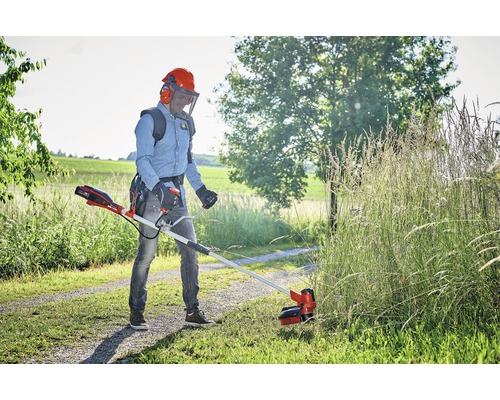 Un homme coupe l''herbe avec un coupe-bordures à batterie dans le jardin.