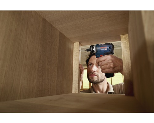 Un homme visse une étagère en bois avec une visseuse sans fil.