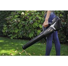 Eine Person hält einen Laubbläser im Garten.