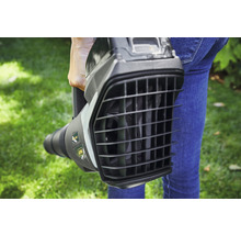 Eine Person hält einen Laubbläser im Garten.