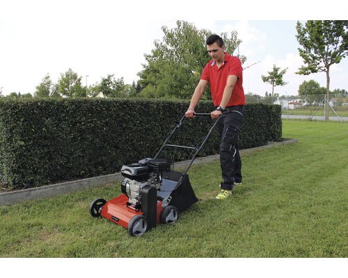 Mann bedient einen Rasenlüfter im Garten.