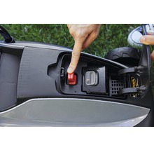 Detailansicht eines Rasenroboters mit Fokus auf den Akku und den roten Sicherheitsschalter, der von einer Hand betätigt wird.