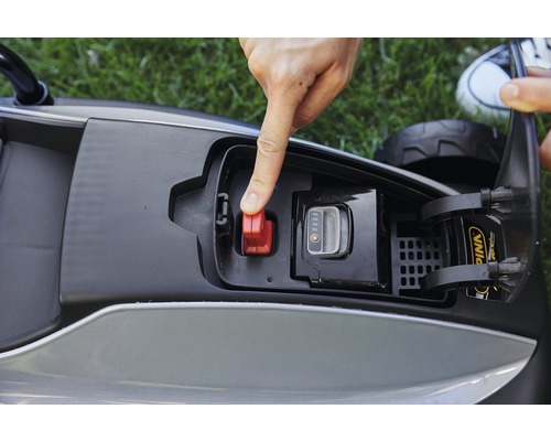 Detailansicht eines Rasenroboters mit Fokus auf den Akku und den roten Sicherheitsschalter, der von einer Hand betätigt wird.