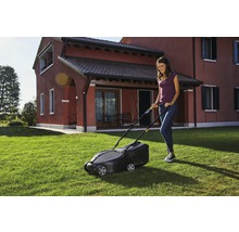 Frau benutzt Rasenmäher im Garten vor Wohnhaus.