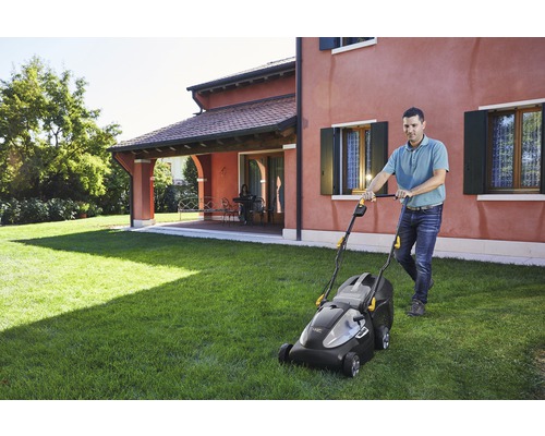 Mann mäht Rasen mit einem Rasenmäher vor einem Wohnhaus.