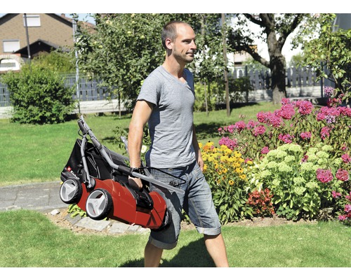 Eine Person trägt einen Vertikutierer durch einen Garten.