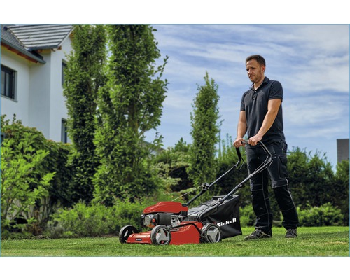Un homme utilise une tondeuse à gazon à essence rouge Einhell dans le jardin.