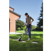 Frau benutzt einen Akku-Rasentrimmer im Garten.