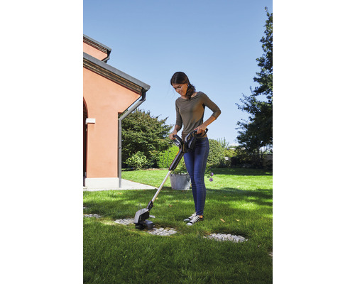 Frau benutzt einen Akku-Rasentrimmer im Garten.