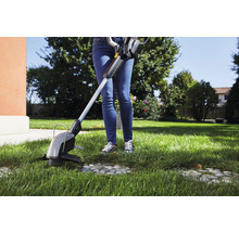 Eine Person schneidet Gras mit einem Rasentrimmer im Garten.