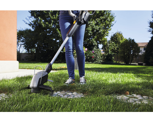 Eine Person schneidet Gras mit einem Rasentrimmer im Garten.