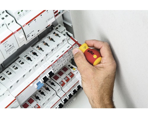 Eine Hand benutzt einen Schraubendreher an einem Sicherungskasten mit ABB-Komponenten.