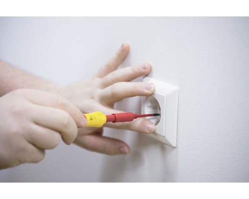 Eine Hand führt mit einem Schraubendreher Elektroarbeiten an einer Steckdose durch.