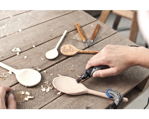 Handwerksszene mit Holzlöffeln, Schnitzwerkzeugen und rotierendem Werkzeug auf einer Holzoberfläche