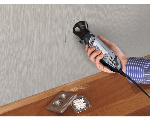 Une personne utilise un outil Dremel pour découper une cavité dans un mur, avec une prise électrique à proximité.