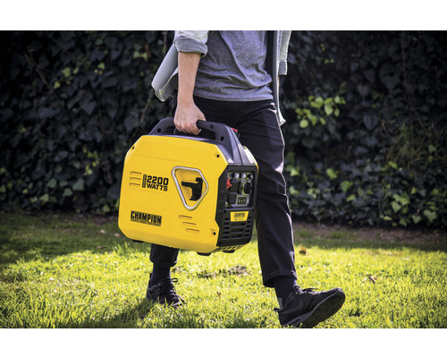 Une personne porte un générateur électrique Champion jaune de 2200 watts dans le jardin.