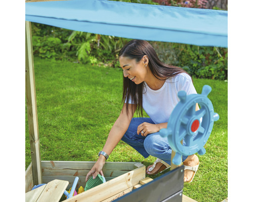 Frau spielt mit Sandspielzeug in einem Sandkasten mit Sonnenschutz