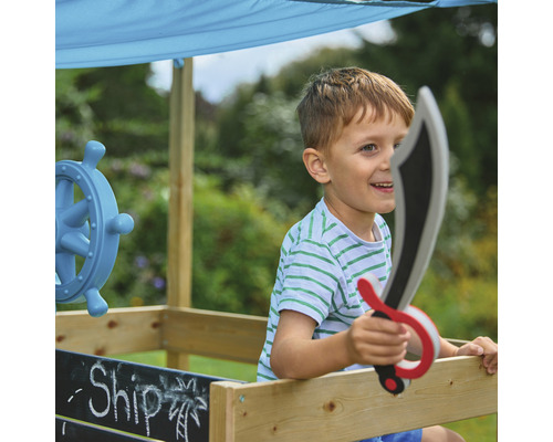 Junge spielt mit einem Spielschiff und einem Spielzeugschwert im Garten