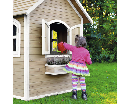 Une fille arrose des fleurs devant une cabane de jeux en bois dans le jardin