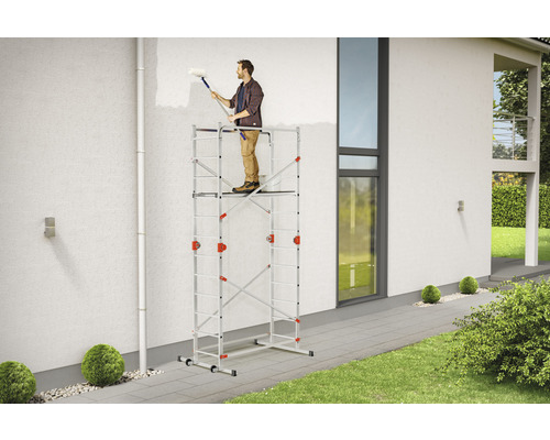 Mann streicht Hauswand stehend auf einem Rollgerüst