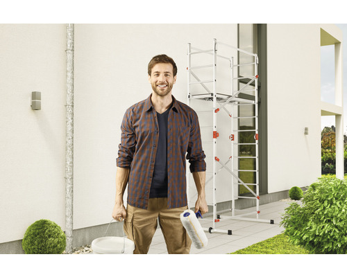 Mann mit Farbeimer und Farbroller vor einem Fassadengerüst