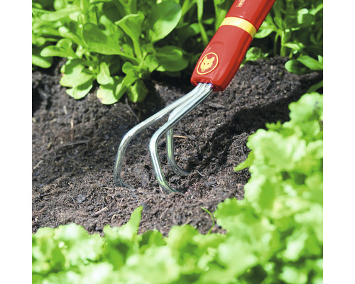 Logo Wolf Garten. Griffe de jardin en cours d''utilisation pour ameublir le sol.