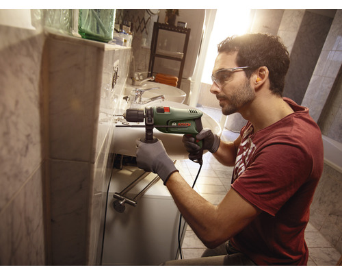 Mann bohrt mit einer Bohrmaschine in einem Badezimmer