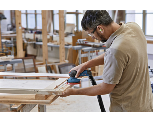 Un homme ponce un cadre en bois avec une ponceuse excentrique dans un atelier.