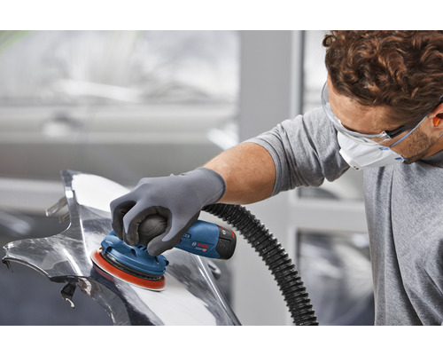 Un homme ponce une pièce métallique à l''aide d''une ponceuse excentrique.