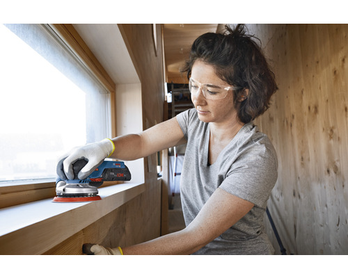 Frau schleift Fensterrahmen mit einem Exzenterschleifer