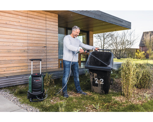 Un homme nettoie une poubelle avec un nettoyeur haute pression dans le jardin.