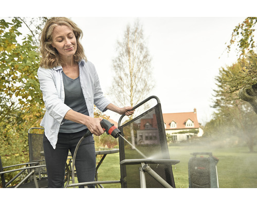 Femme nettoie les meubles de jardin avec un nettoyeur haute pression à l'extérieur