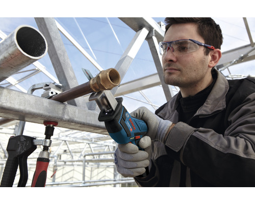 Un homme scie un tuyau avec une scie sabre Bosch, tout en portant des lunettes de protection et des gants.