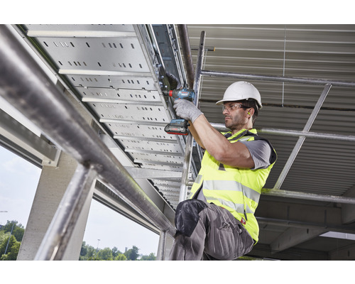 Un homme monte un chemin de câbles avec une visseuse sans fil.