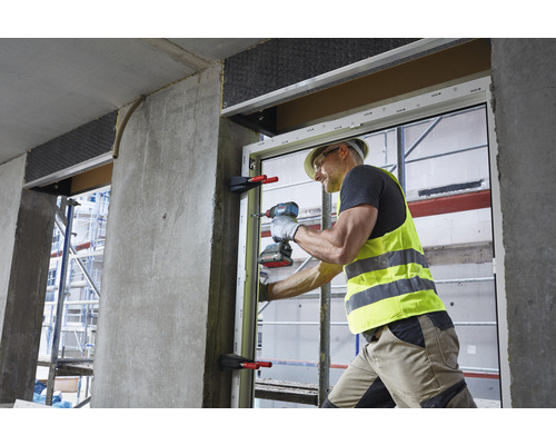 Un ouvrier monte une fenêtre dans un bâtiment à l'aide d'une visseuse sans fil.