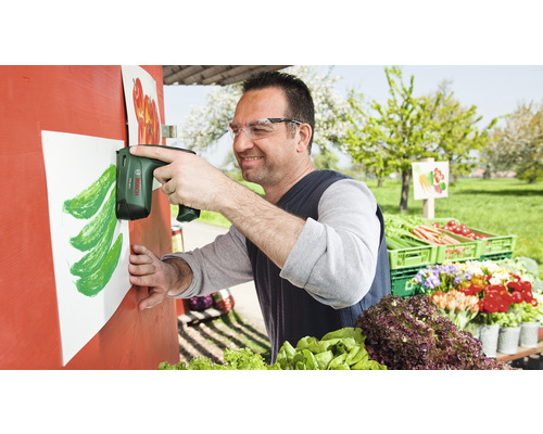 Un homme fixe une feuille de papier sur un étal de vente de légumes à l''aide d''une agrafeuse sans fil.