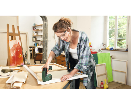 Femme tend une toile avec une agrafeuse électrique dans un atelier lumineux