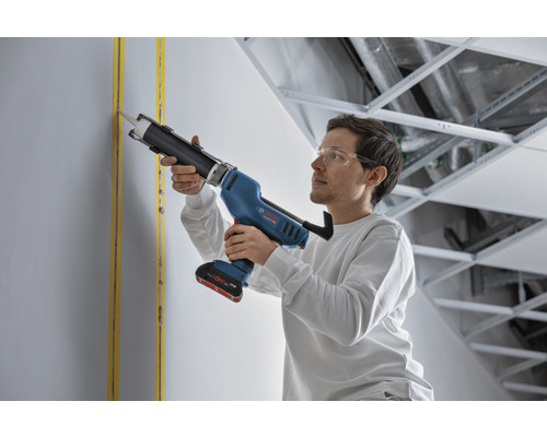 Un homme utilise un pistolet à cartouche sans fil Bosch pour jointoyer un mur.
