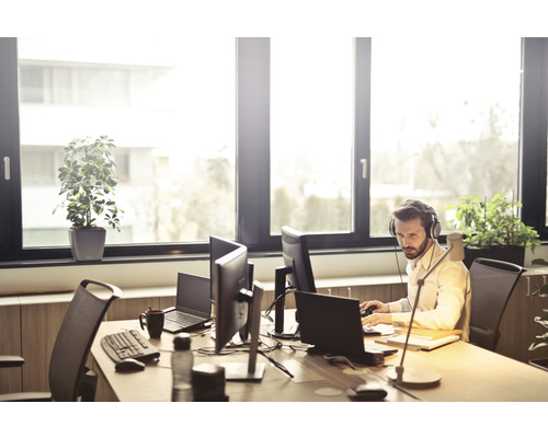 Scène de bureau avec une personne, des ordinateurs, des plantes et des fournitures de bureau sur un bureau.