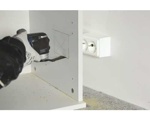 Une personne découpe un trou dans un morceau de bois à l''aide d''un outil multifonction près d''une prise électrique.