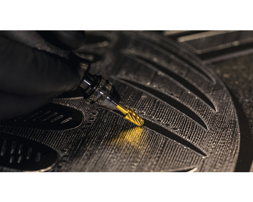 Gros plan d''une main tenant un burin qui grave des détails dans une pièce.