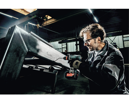 Ein Mann bohrt mit einem Akku-Bohrschrauber ein Loch in ein Metallstück.