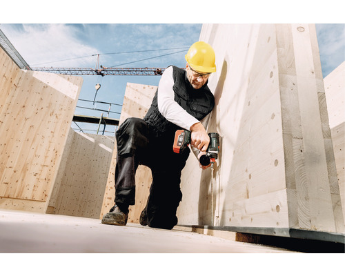 Ein Bauarbeiter mit Schutzhelm montiert eine Holzkonstruktion mit einem Akkuschrauber.