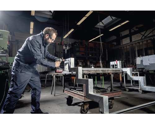 Ein Mann bohrt mit einer Bohrmaschine in einem Werkstück in einer Werkstatt.