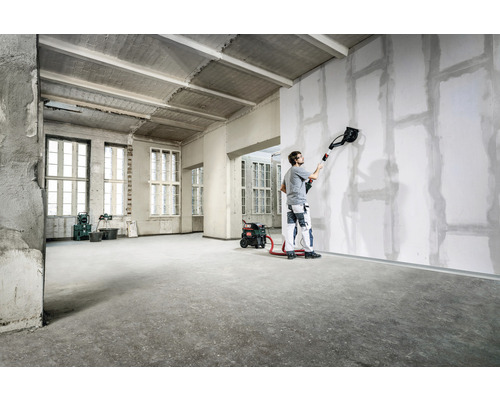 Ein Mann verwendet eine Trockenbau Schleifmaschine in einem Raum, um Wände zu glätten.